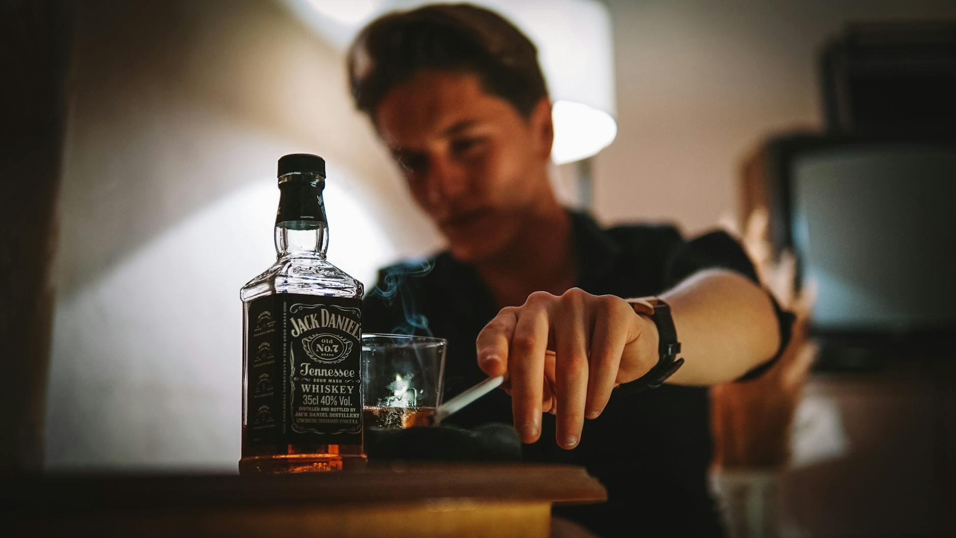 a man smoking a cigarette while drinking a bottle of Jack Daniels and smoking a cigarette