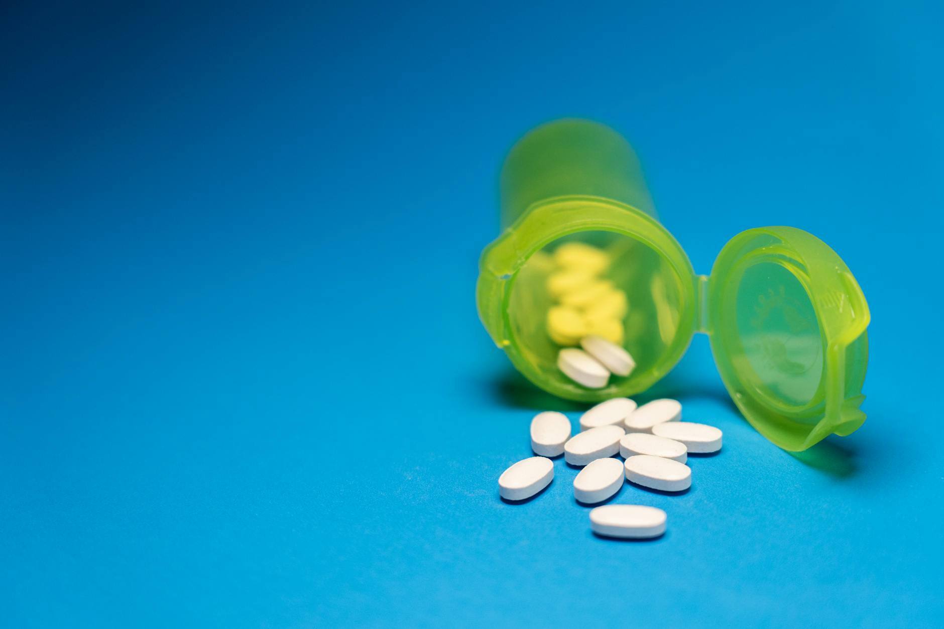 open green pill bottle with white tablets on blue surface
